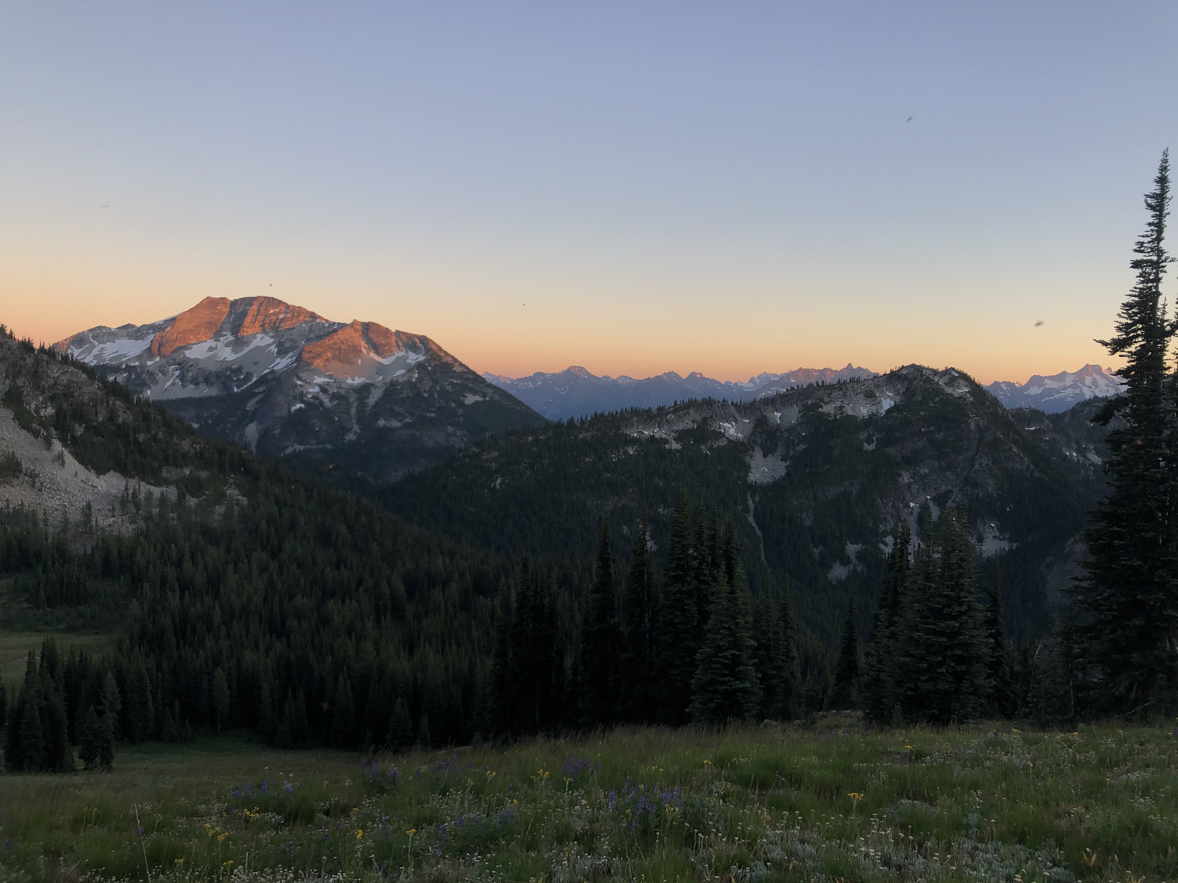 A mountain range is lit up from behind by a sunset fading from an orange to blue sky at the top of the photo. 
