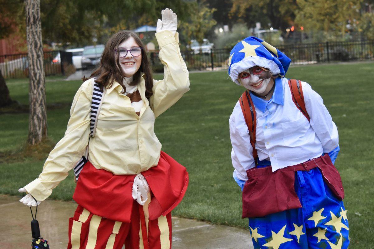 Macphee and Herber pose wearing colorful, patterned pants and button-up shirts. Their faces are painted black and white. 