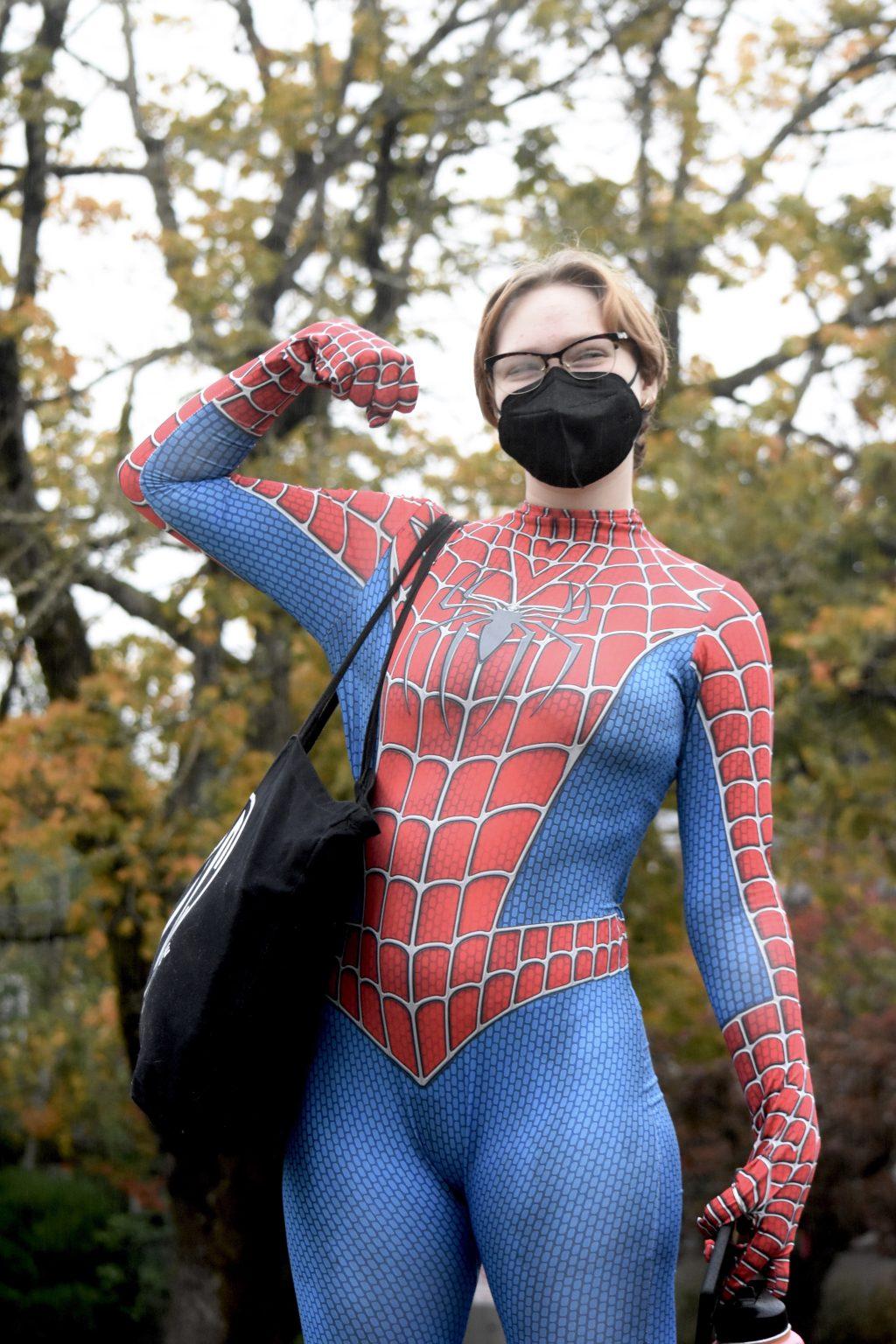 Wilmart stands in front of a tree, wearing a blue and red Spiderman suit and posing with his bicep flexed. 