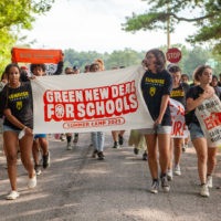 Youth activists march holding a large poster with the words "Green New Deal for Schools."